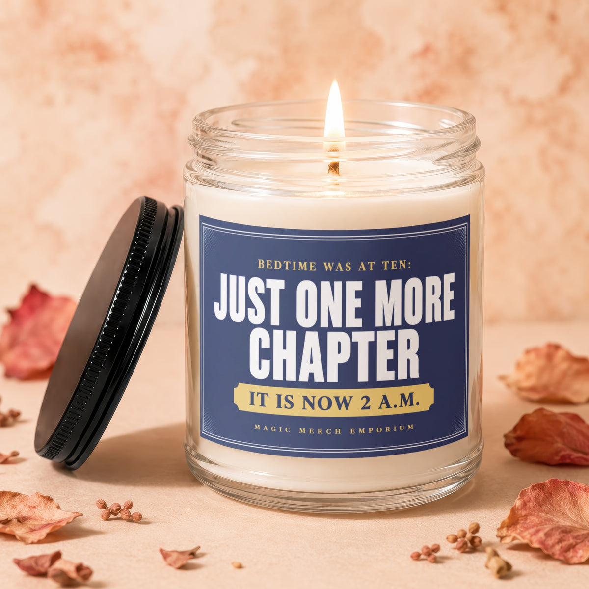 Lit candle with "Just One More Chapter" text, lid off, surrounded by dried leaves.