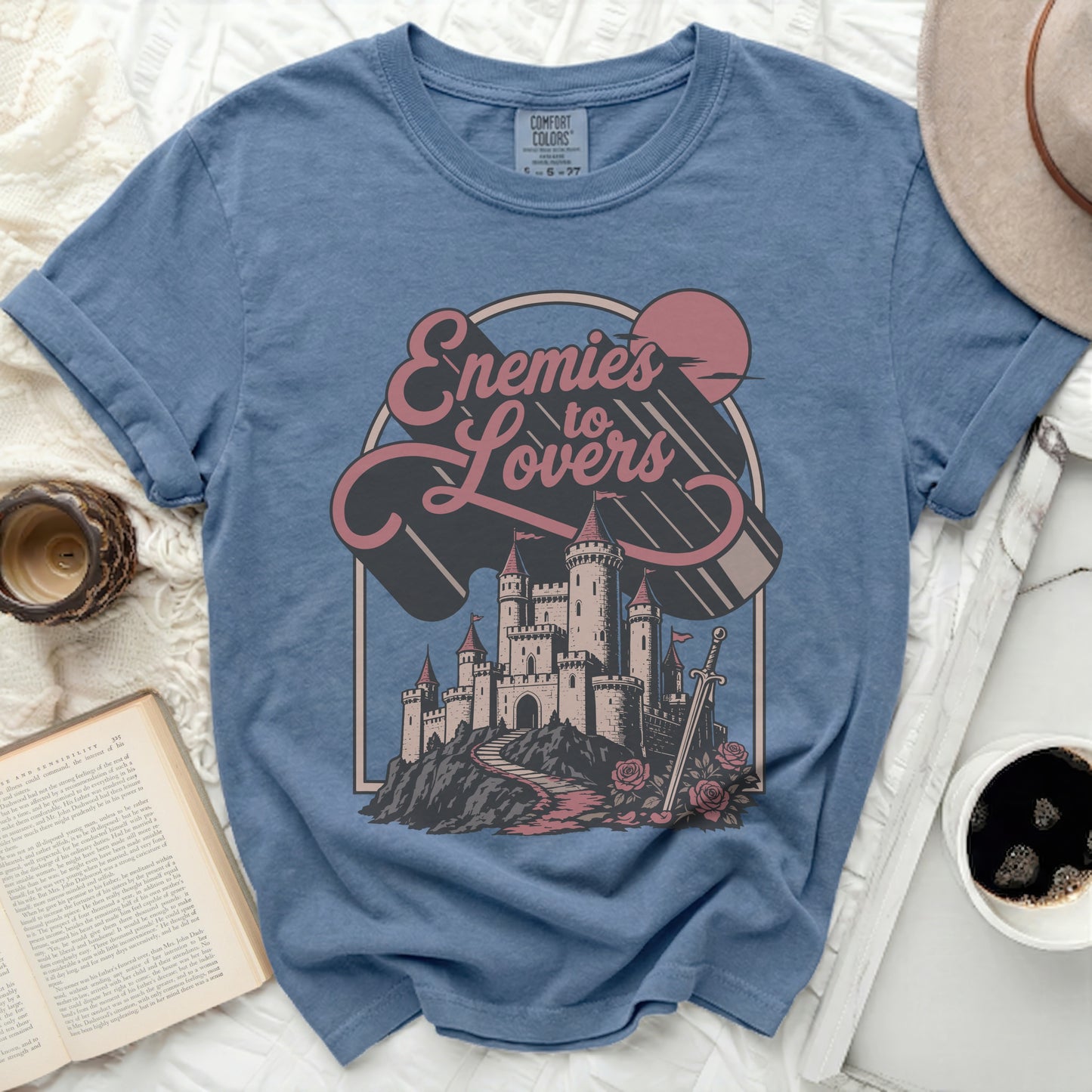 Blue t-shirt with "Enemies to Lovers" graphic featuring castle, sword, roses, and sun.
