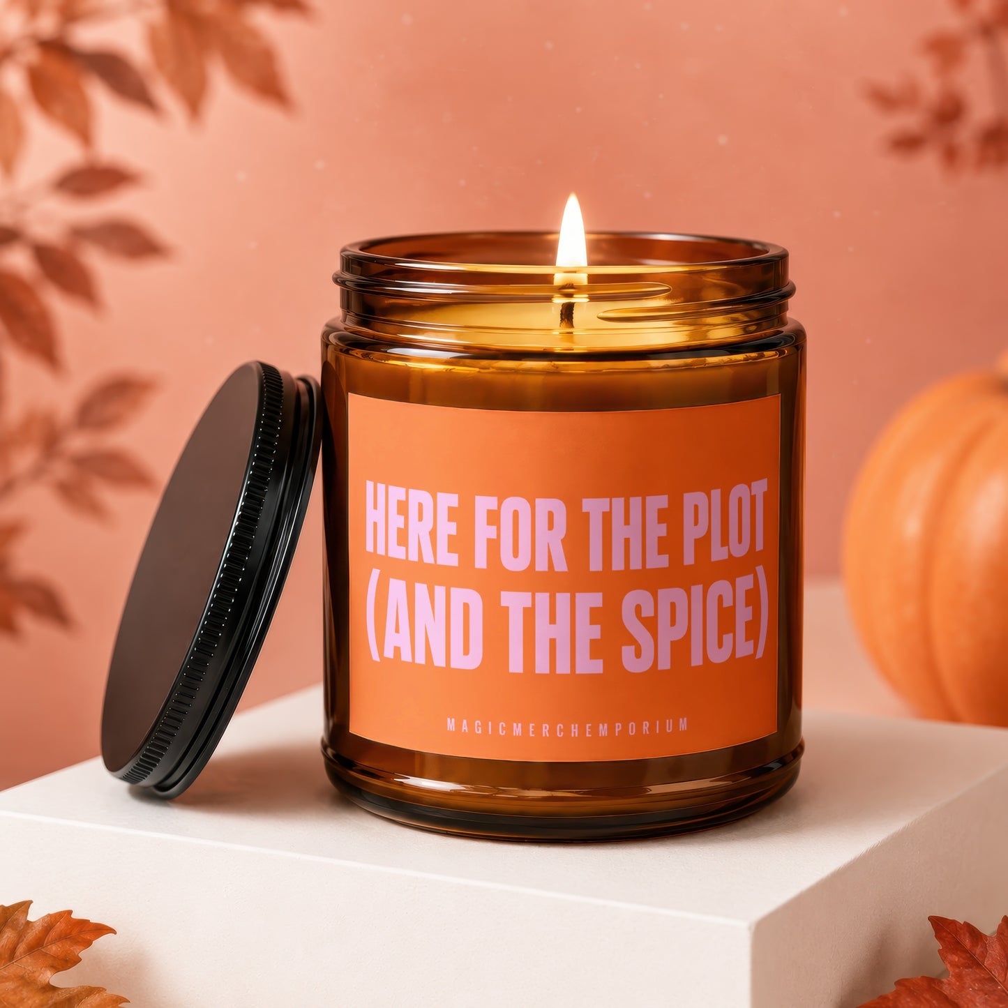 Lit amber candle with orange label reading "HERE FOR THE PLOT (AND THE SPICE)".