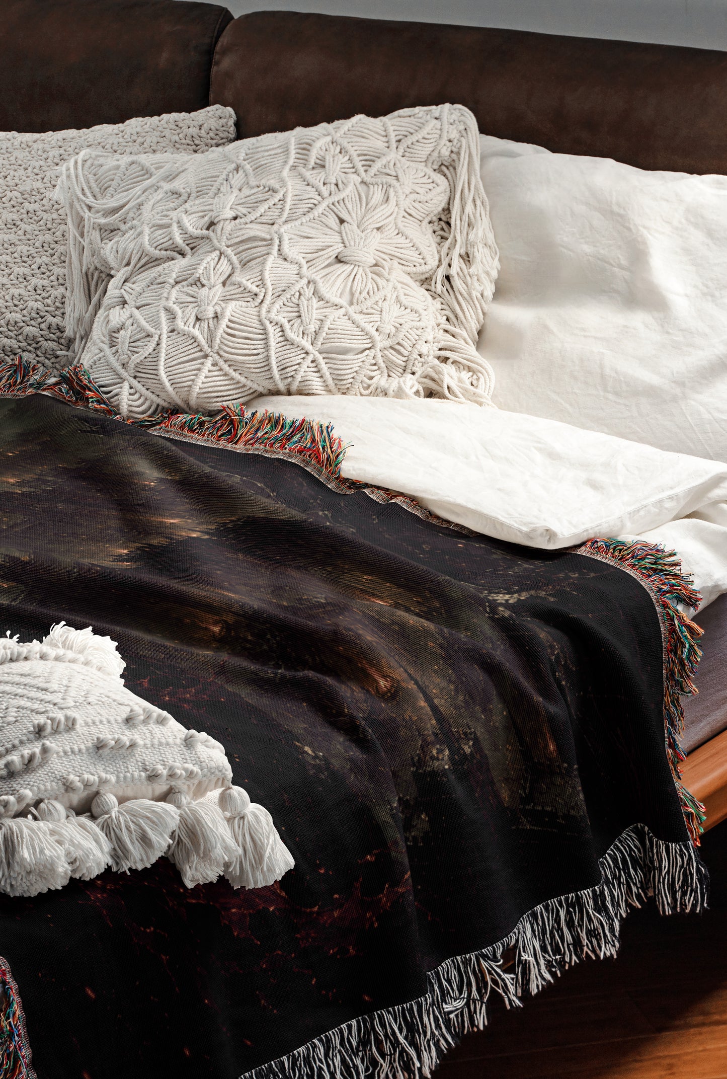 a cozy and inviting bedroom scene, featuring a bed with a black blanket and white pillows, a brown leather couch, and a colorful throw blanket.