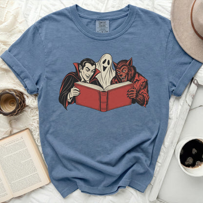 Vampire, ghost, and werewolf reading a red book graphic on a blue t-shirt.