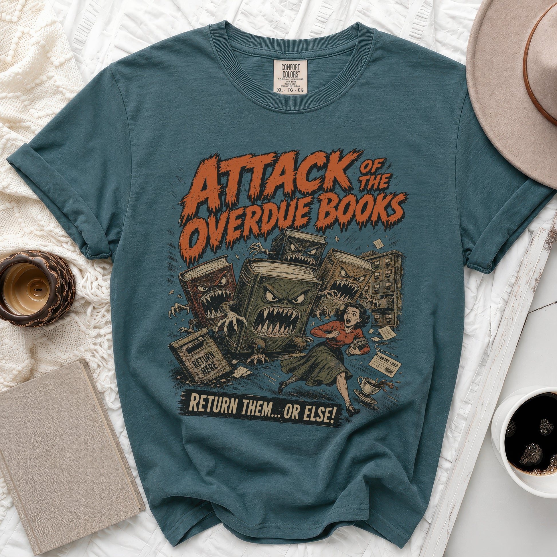 Teal t-shirt with "Attack of the Overdue Books" text and a scene of books chasing a woman.
