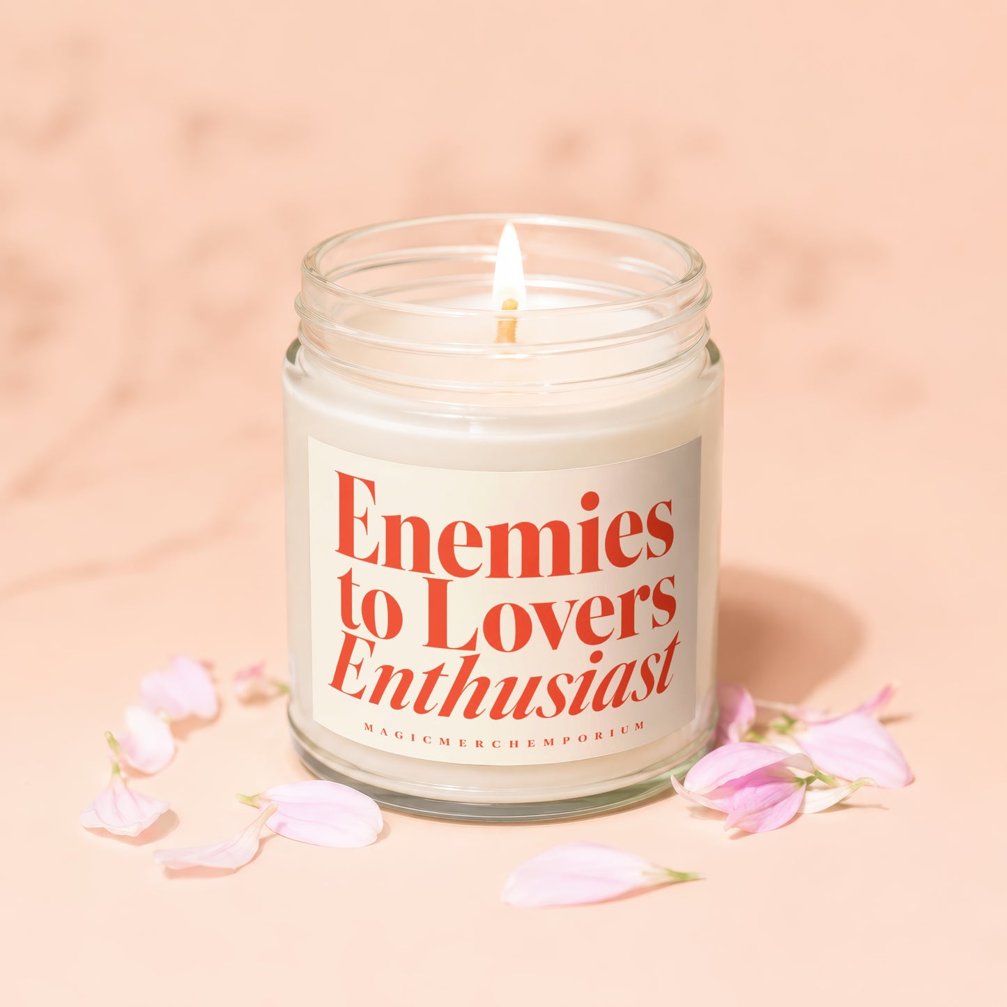 Burning candle in glass jar with "Enemies to Lovers Enthusiast" text and pink petals.