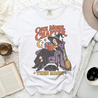 White t-shirt with graphic of witch reading, broom, cat, and text "One More Chapter Then Magic".