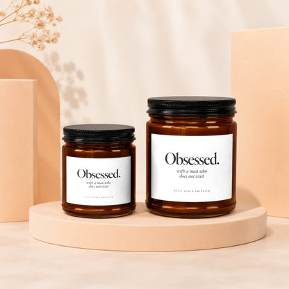 Two amber glass candles labeled "Obsessed. with a man who does not exist."