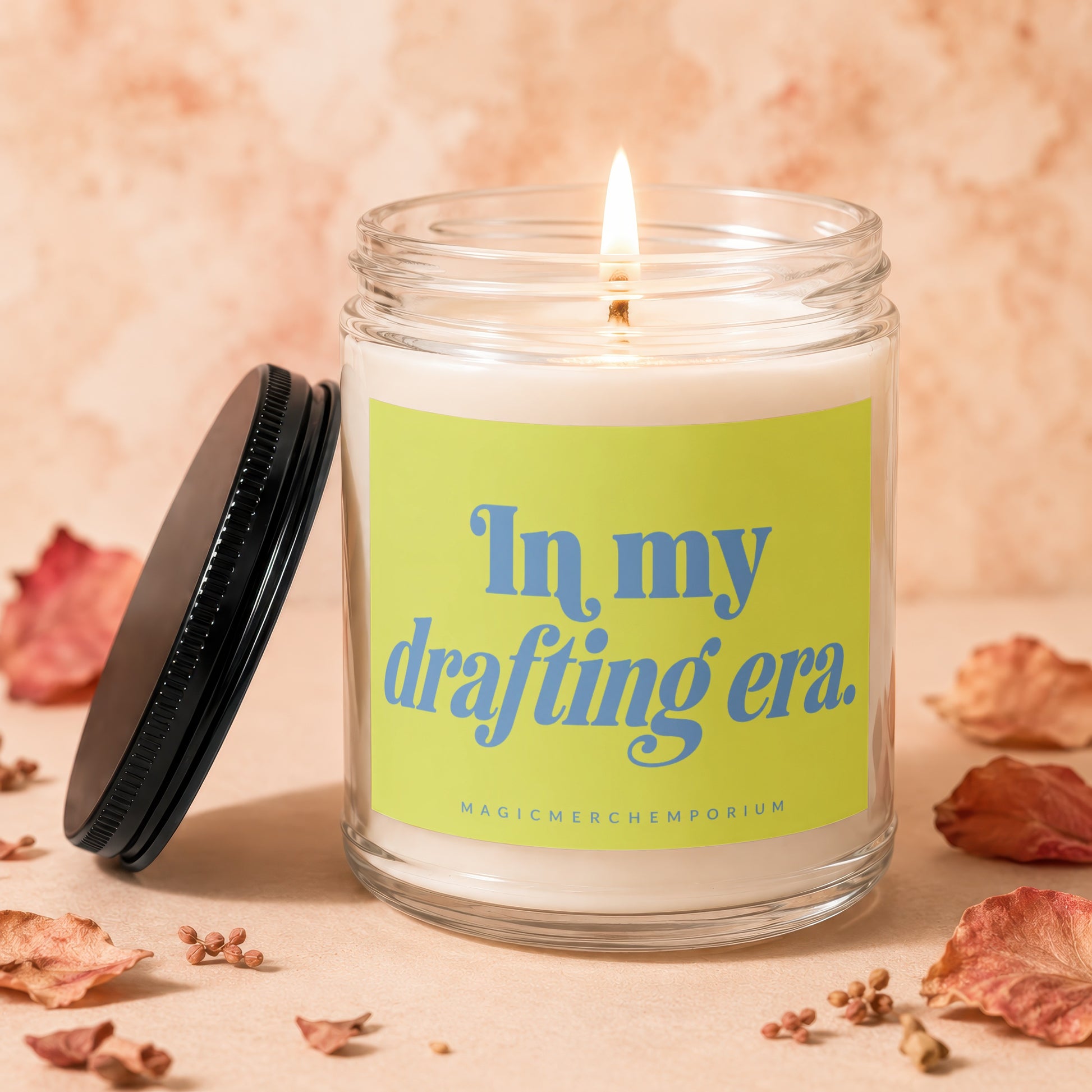 Lit candle in glass jar with "In my drafting era." text on bright green label.