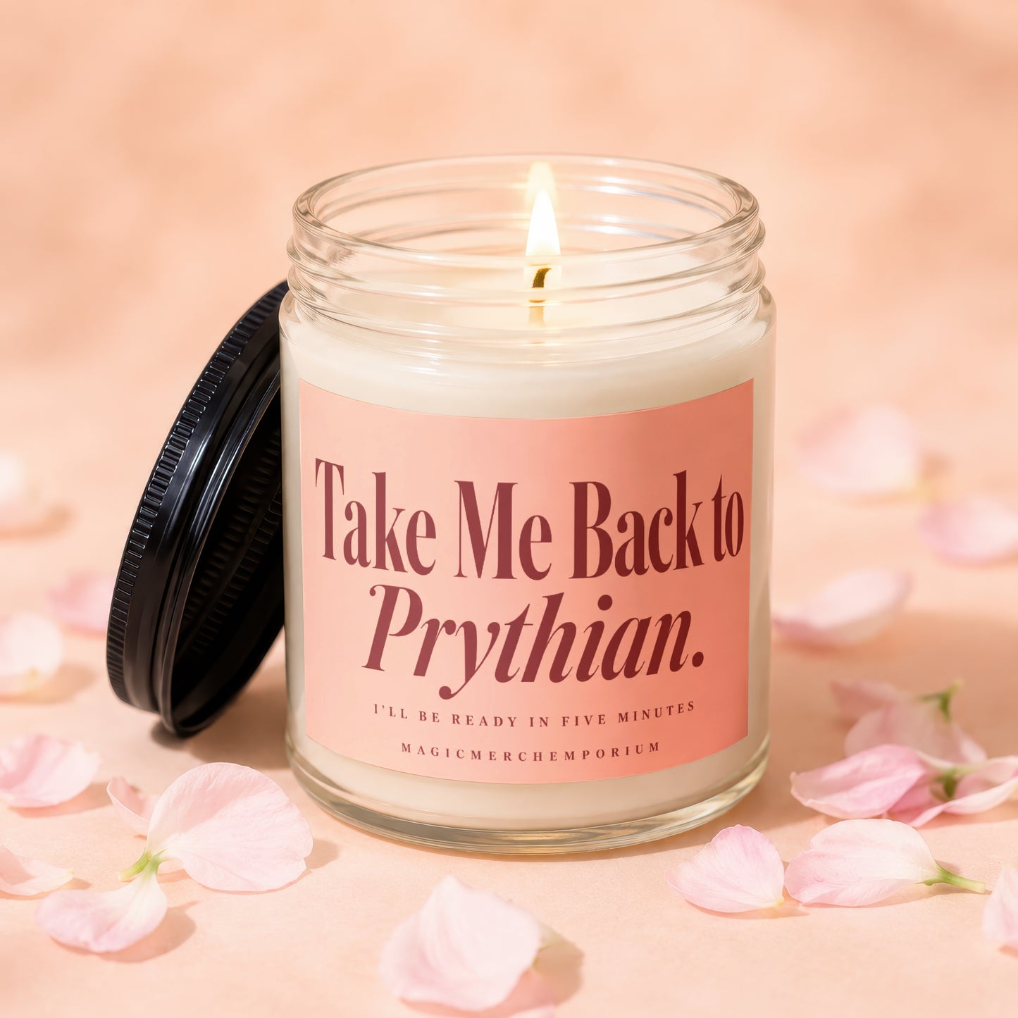A lit candle in a glass jar with a pink label reading Take Me Back to Prythian, surrounded by scattered pink flower petals.