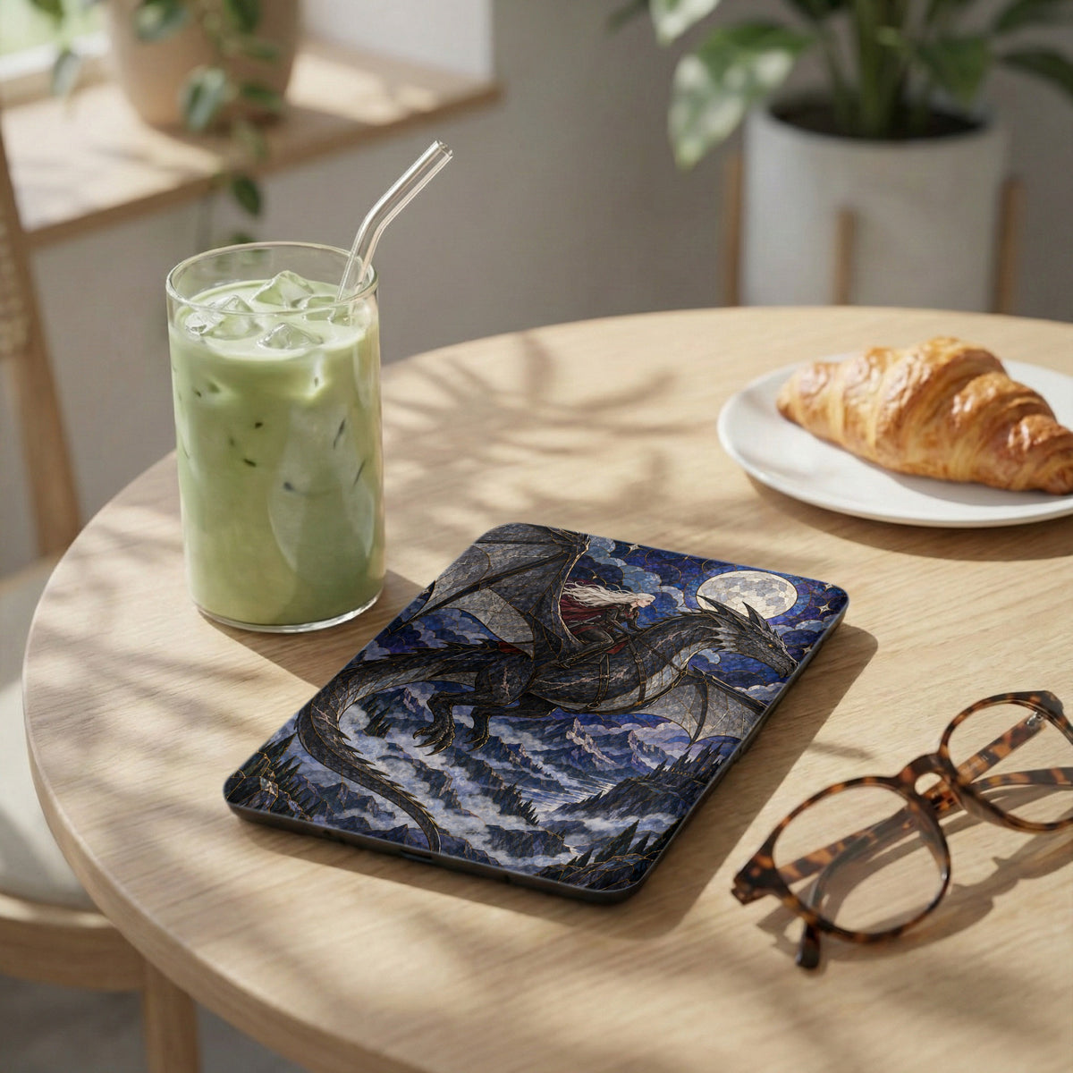 Tablet case with a dragon and rider design, next to a drink and croissant.