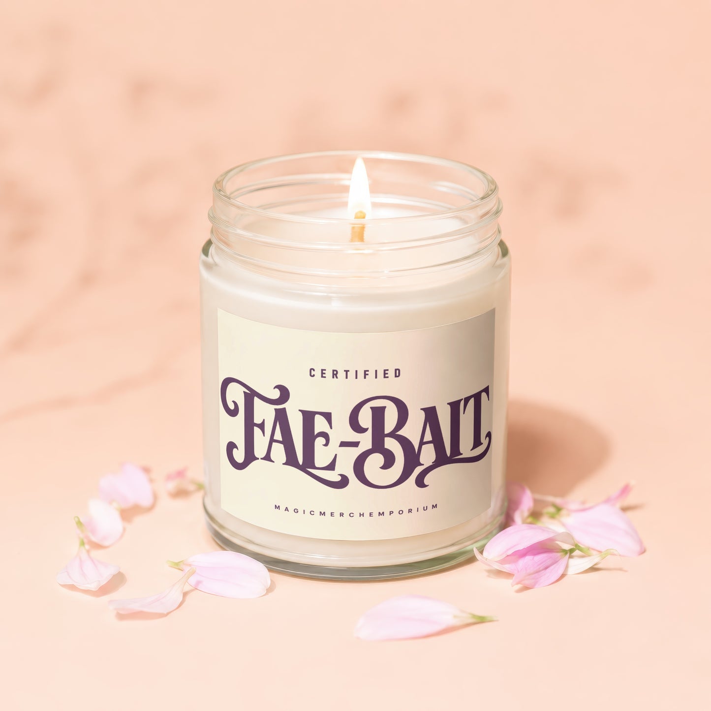 Candle with "Fae-Bait" label, lit wick, and pink petals on peachy background.