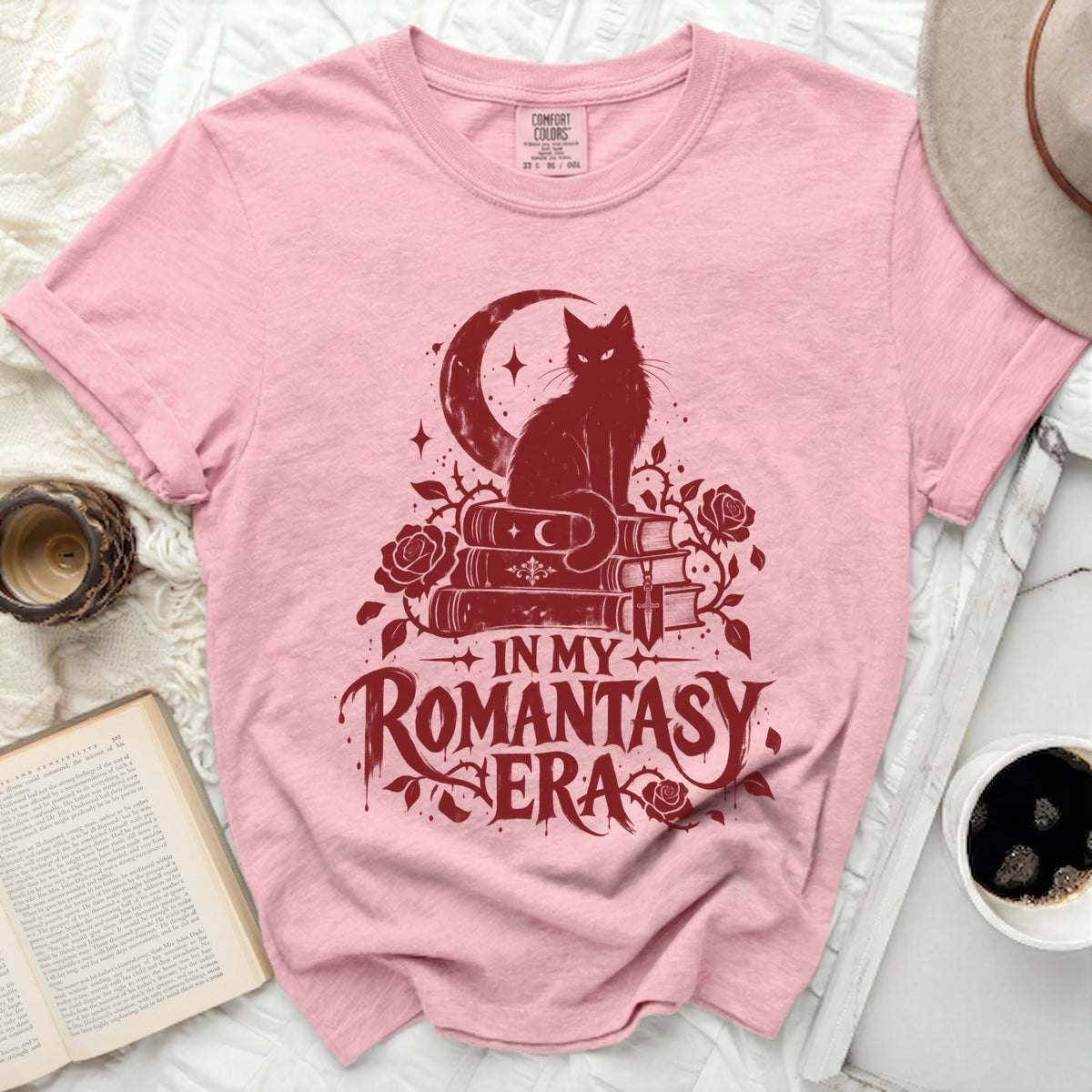 Pink t-shirt with a dark red graphic of a cat on books, moon, roses, and text "In My Romantasy Era".