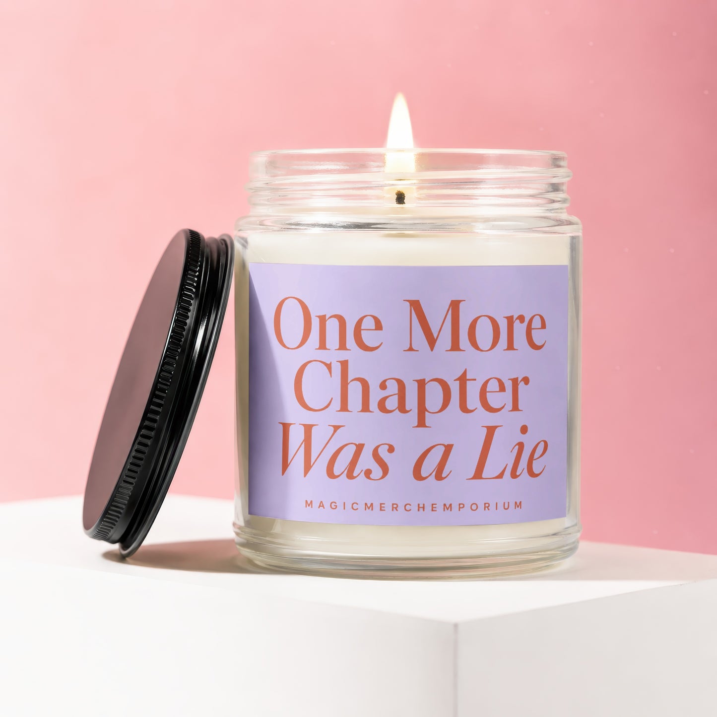 Glass candle with lit wick, black lid, and purple label that reads "One More Chapter Was a Lie."