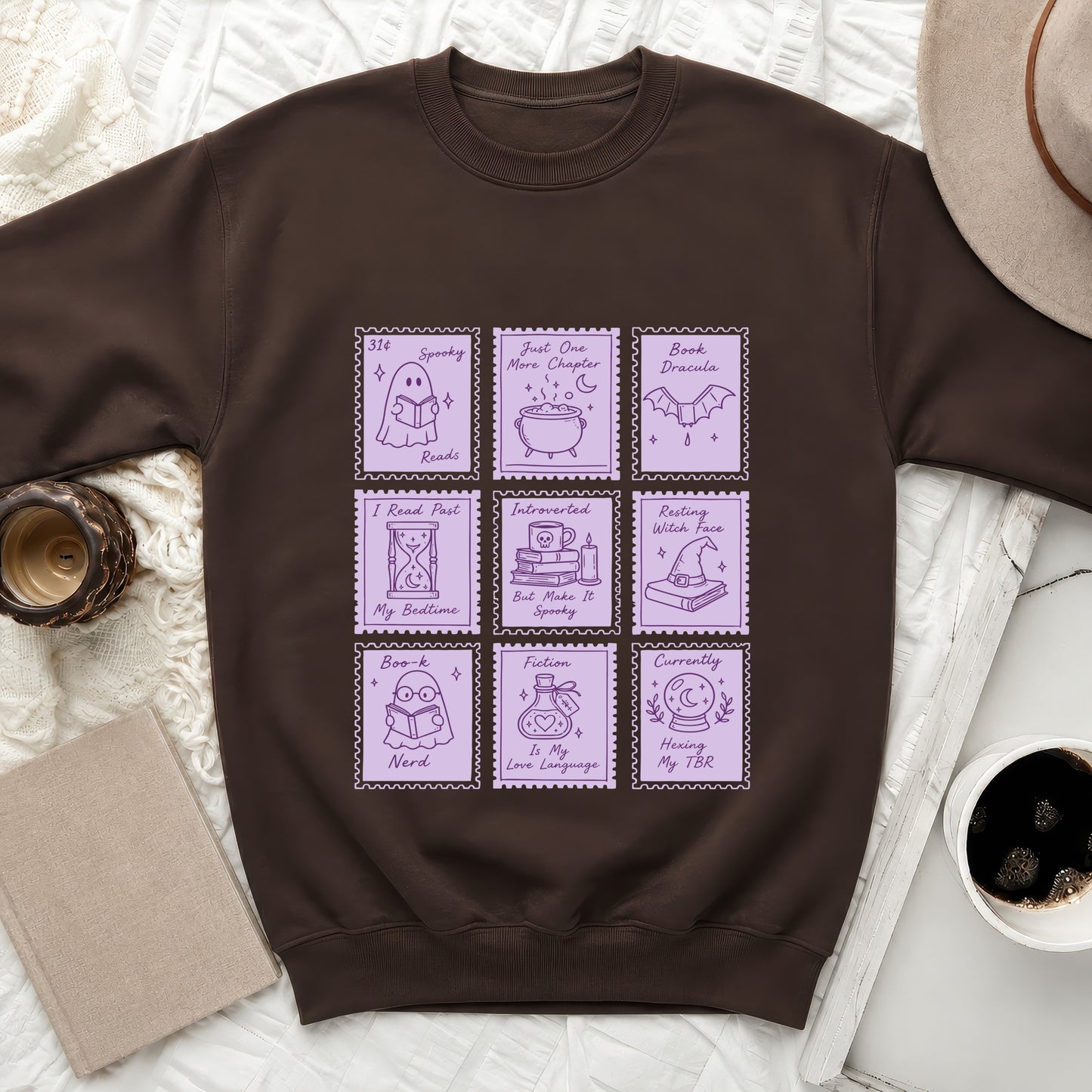 Brown sweatshirt with nine purple stamp designs featuring books and spooky reading themes.