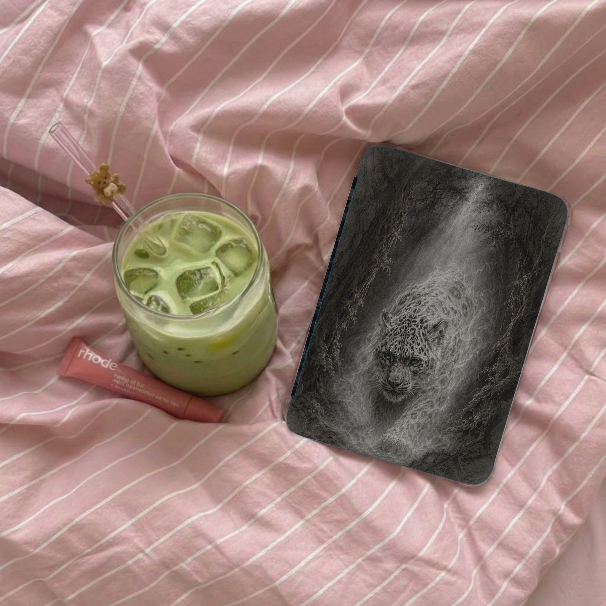 Phone case with a leopard in a forest, beside a matcha drink and lip balm.
