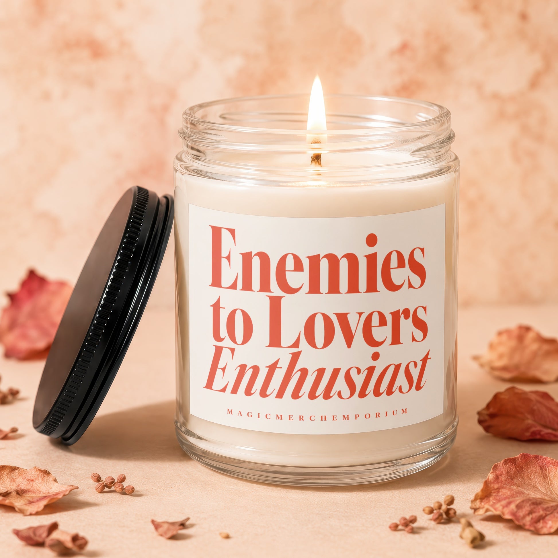 Glass candle with lit wick and label: "Enemies to Lovers Enthusiast"