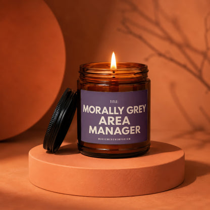 Lit amber glass candle with "Morally Grey Area Manager" text on a purple label.