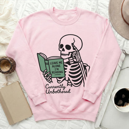 Pink sweatshirt with a skeleton reading a book with "Leave Me Alone I'm Reading" text.