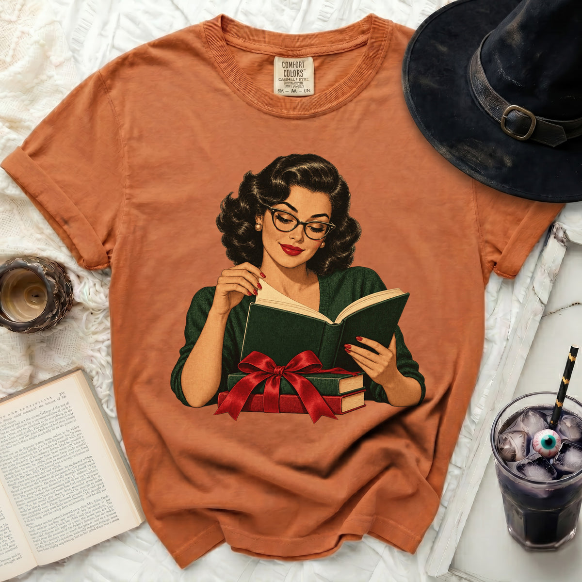Orange t-shirt with a graphic of a woman reading surrounded by books and a red bow.