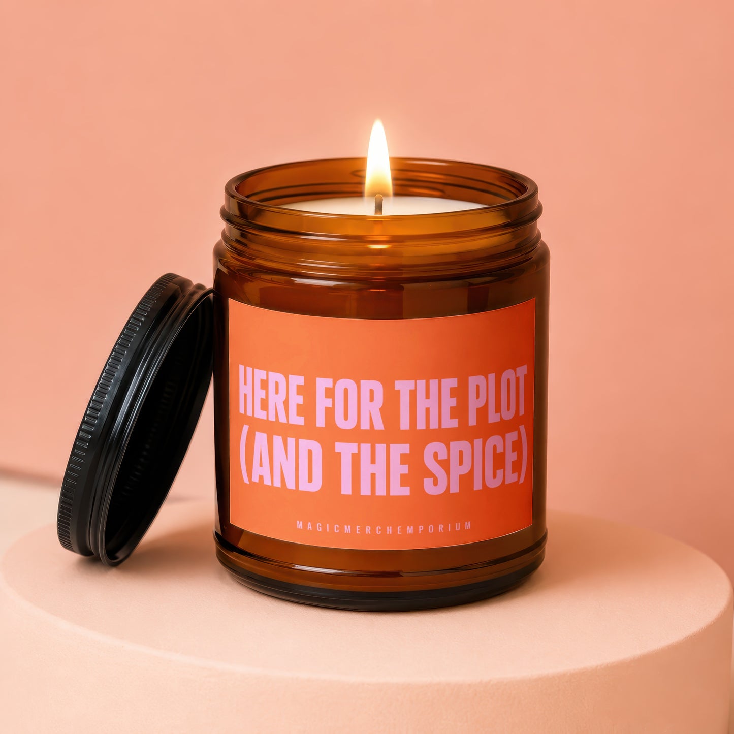 Amber jar candle with burning wick, lid off, reads "Here for the Plot (and the Spice)".