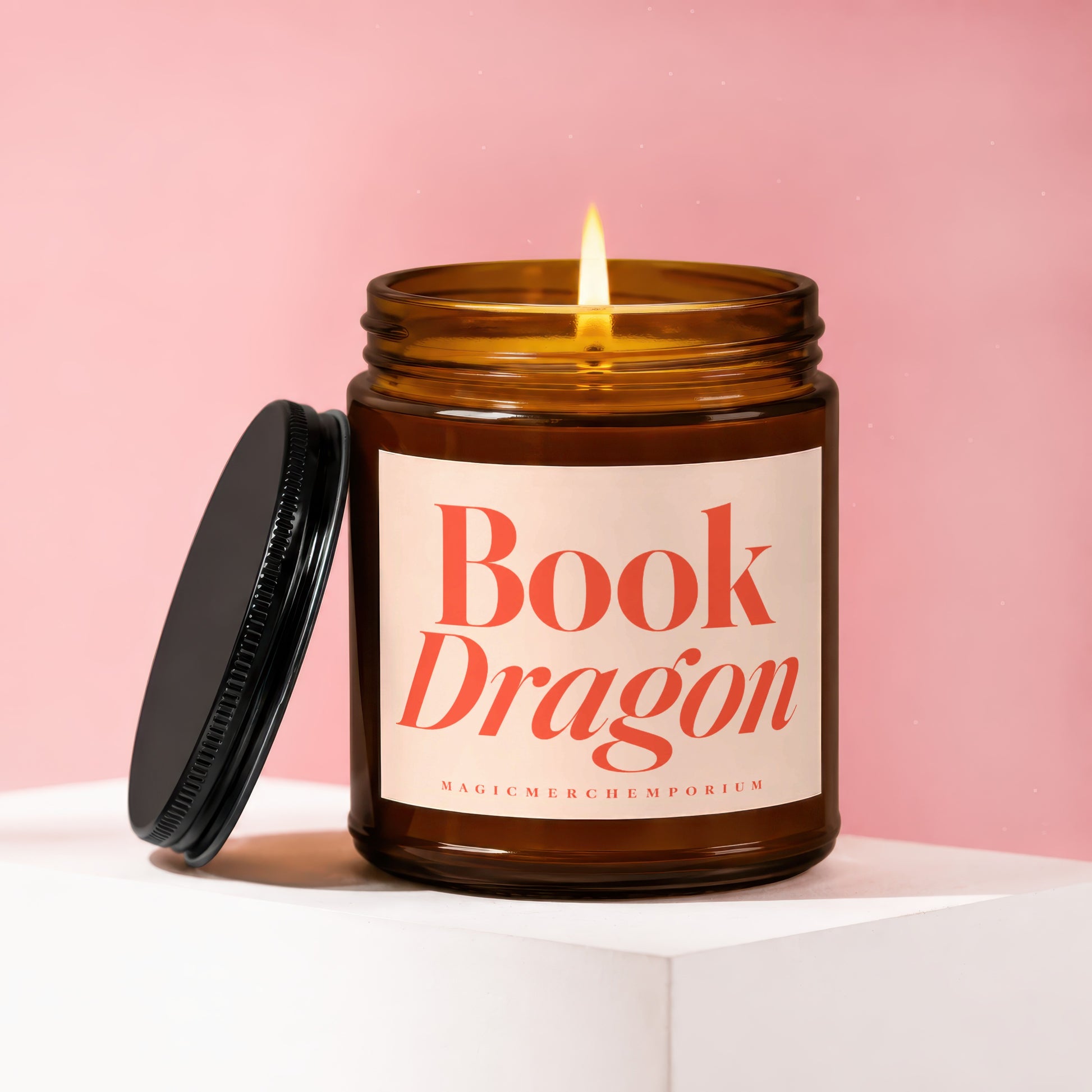 Amber jar candle with lit flame, label reads "Book Dragon" and "MAGICMERCH co.".
