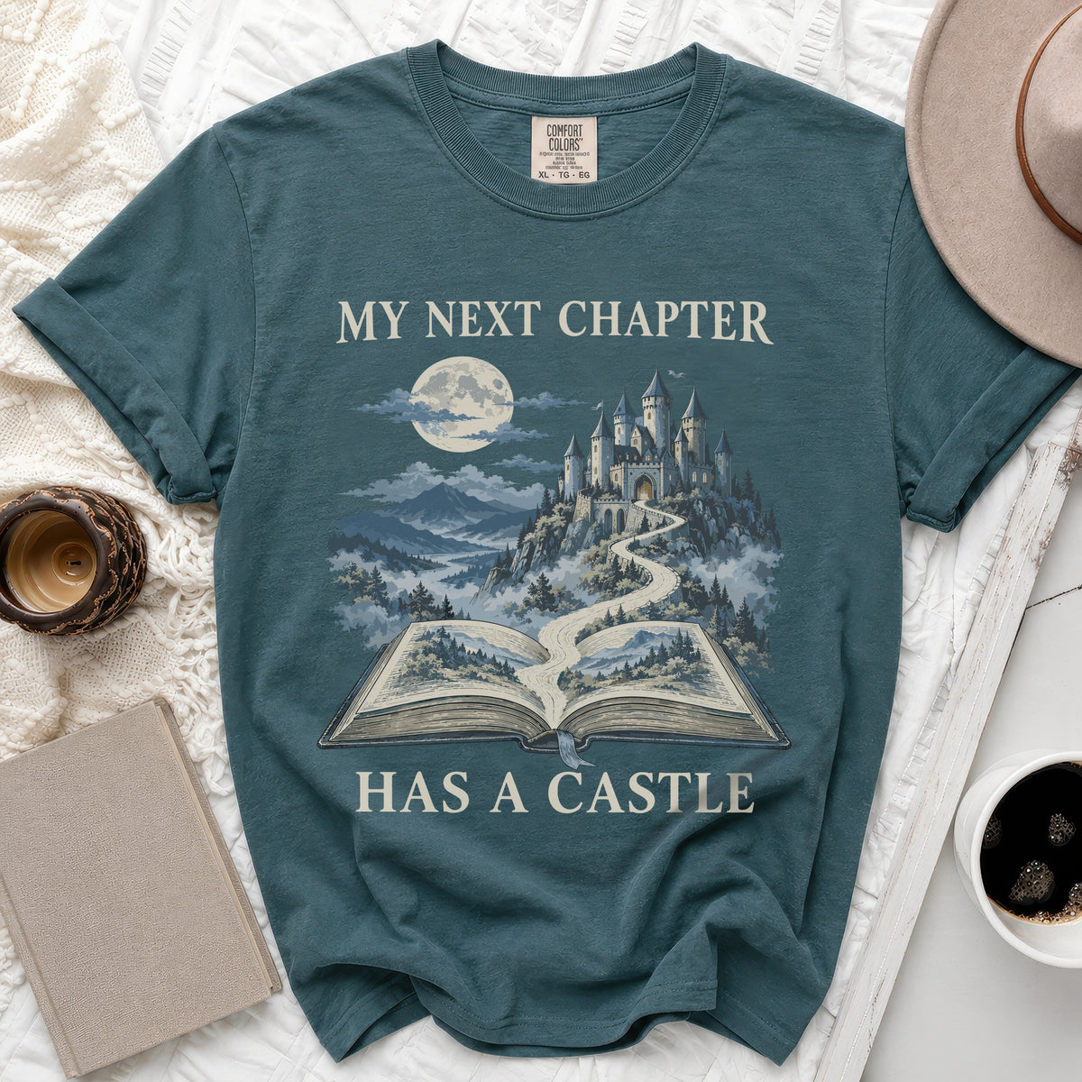 Teal t-shirt with "My Next Chapter Has A Castle" text and castle illustration.