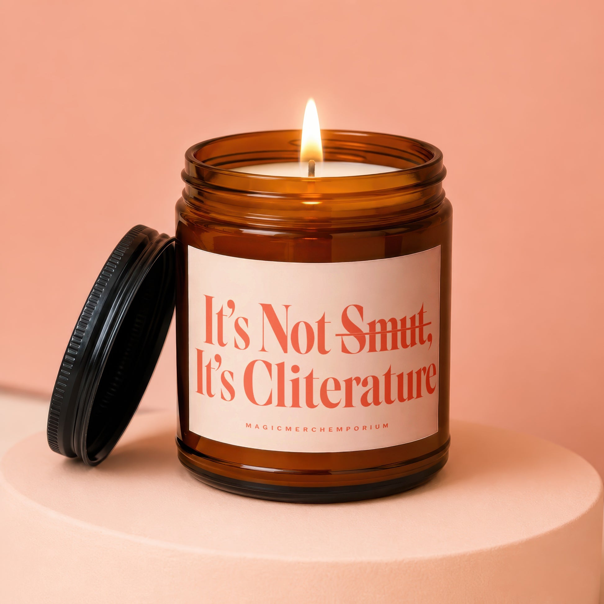 Amber jar candle with lit wick and black lid, labeled "It's Not Smut. It's Cliterature".