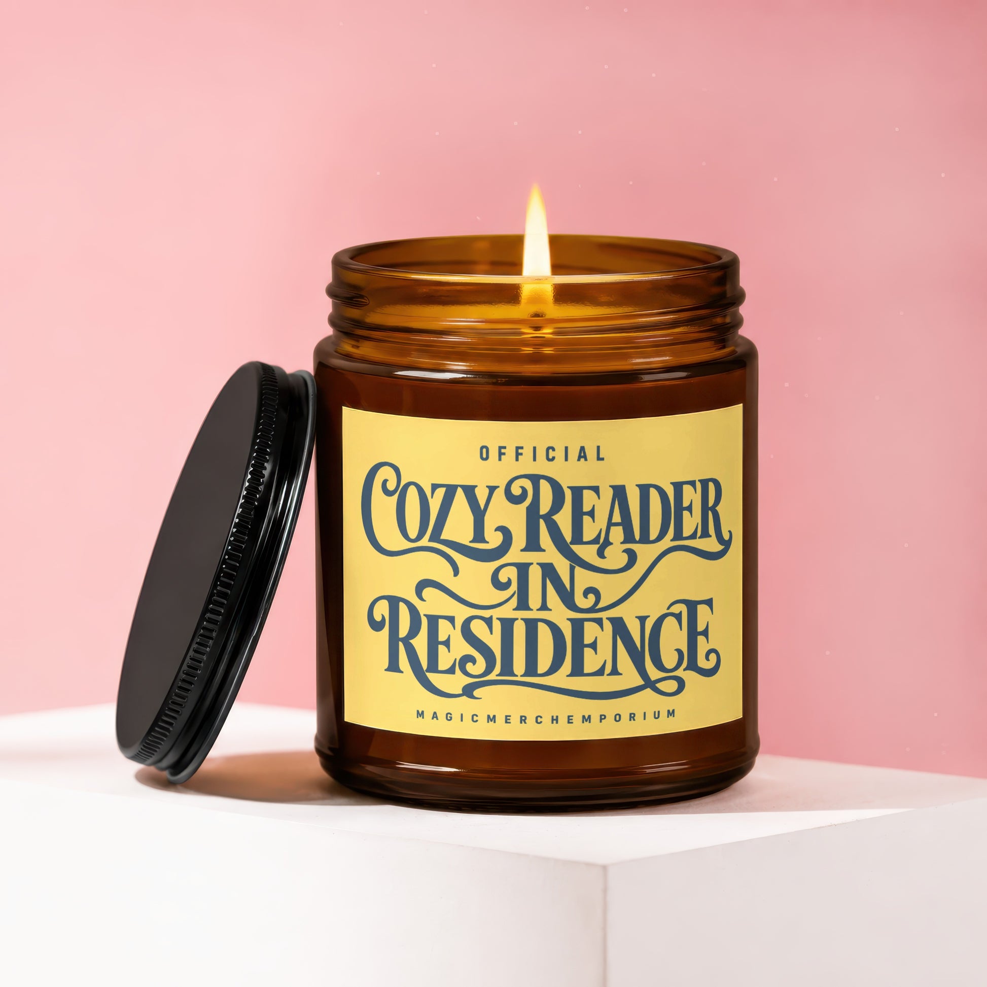 Amber candle with lid off, "Official Cozy Reader In Residence" text on label.