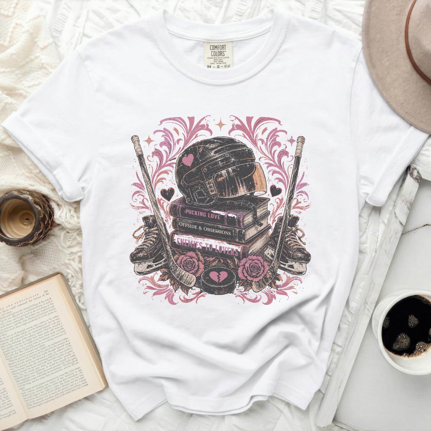 White t-shirt with hockey gear, books, and hearts graphic.