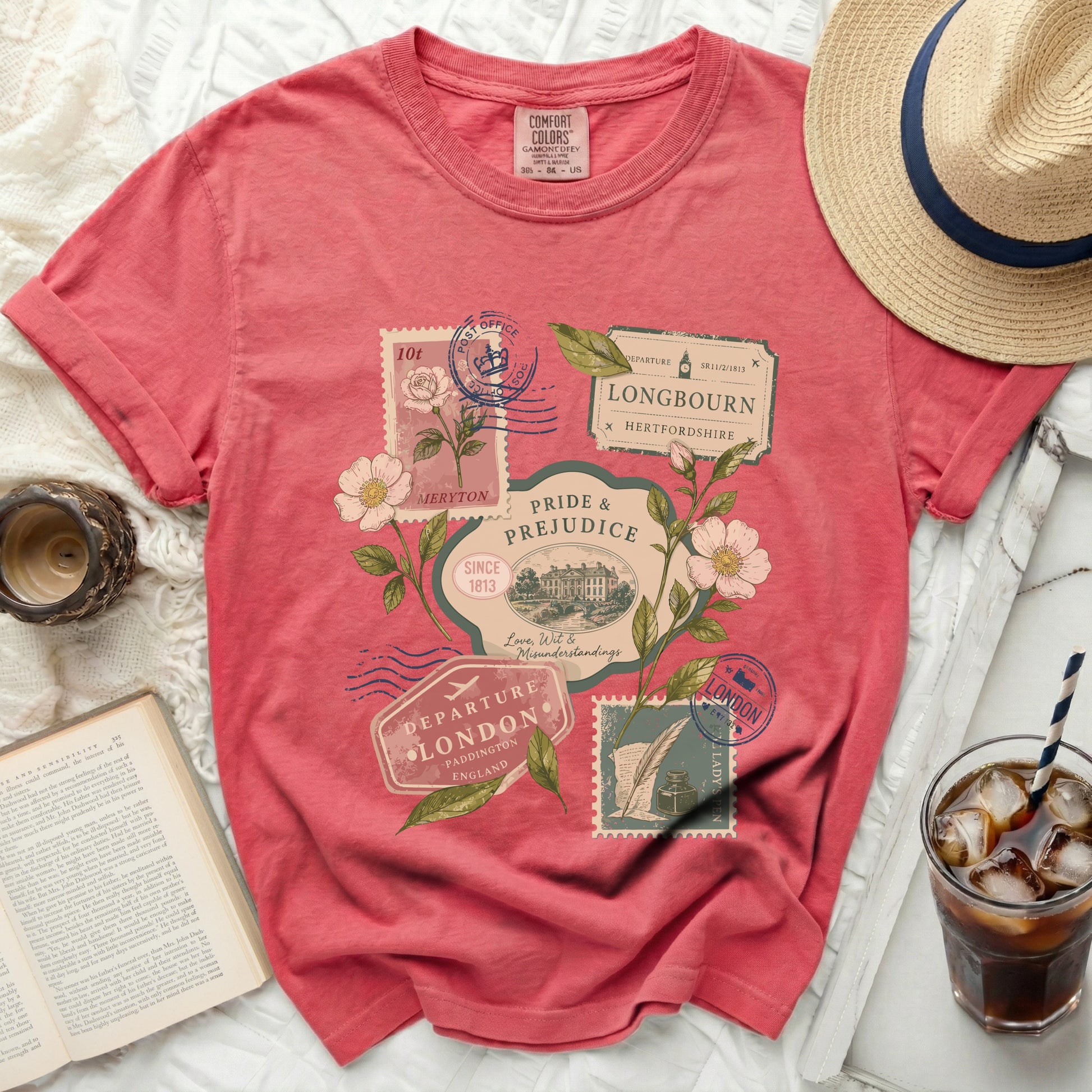 Coral t-shirt with a "Pride & Prejudice" travel stamp graphic and floral elements.