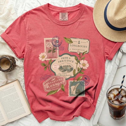 Coral t-shirt with a "Pride & Prejudice" travel stamp graphic and floral elements.