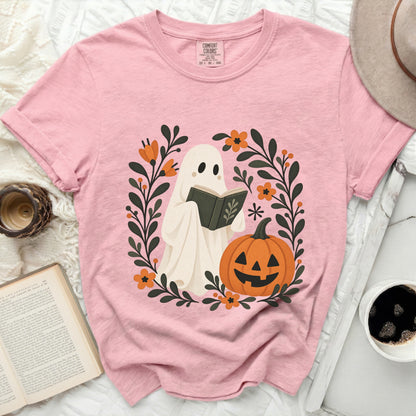 Pink t-shirt with a ghost reading a book surrounded by flowers and a jack-o-lantern.