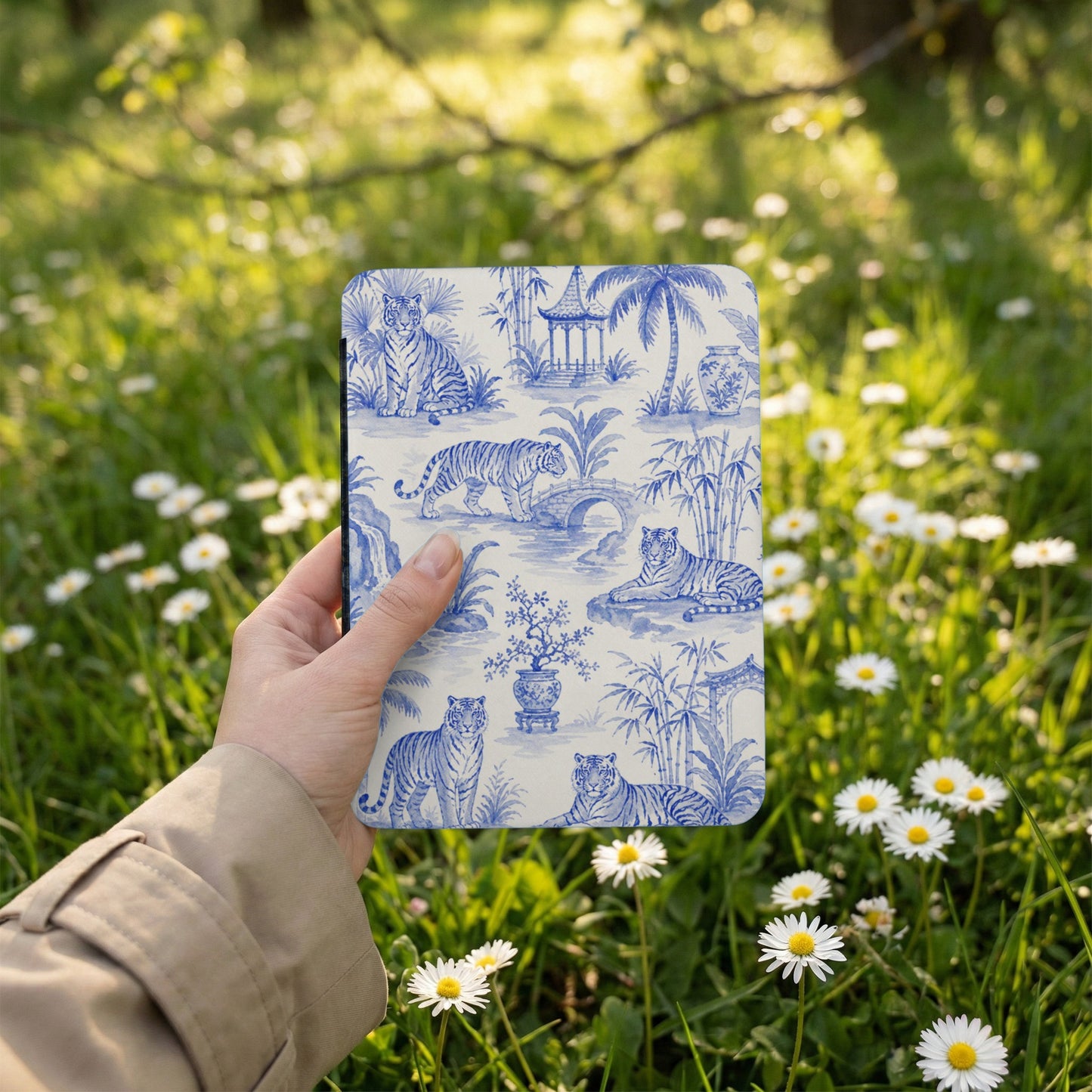 Blue and white toile pattern with tigers, bamboo, and pagodas on a flat object held outdoors.