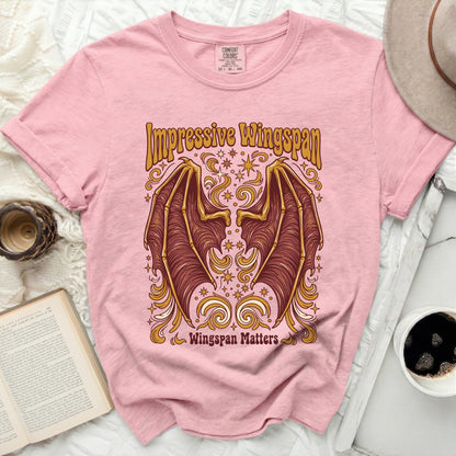 Pink t-shirt with a graphic of bat wings and text "Impressive Wingspan Wingspan Matters".