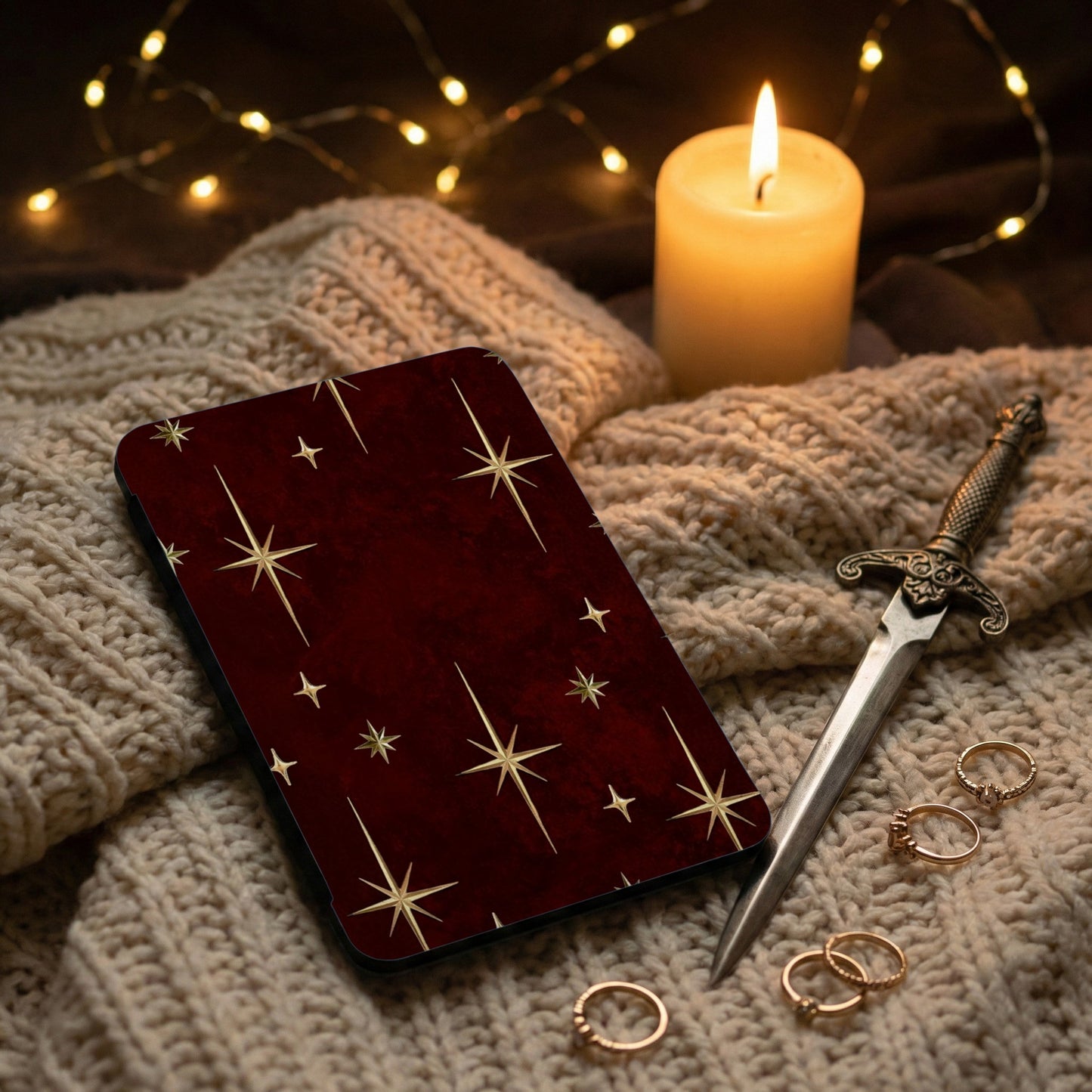 Burgundy case with gold stars, a lit candle, and rings on a knit blanket.