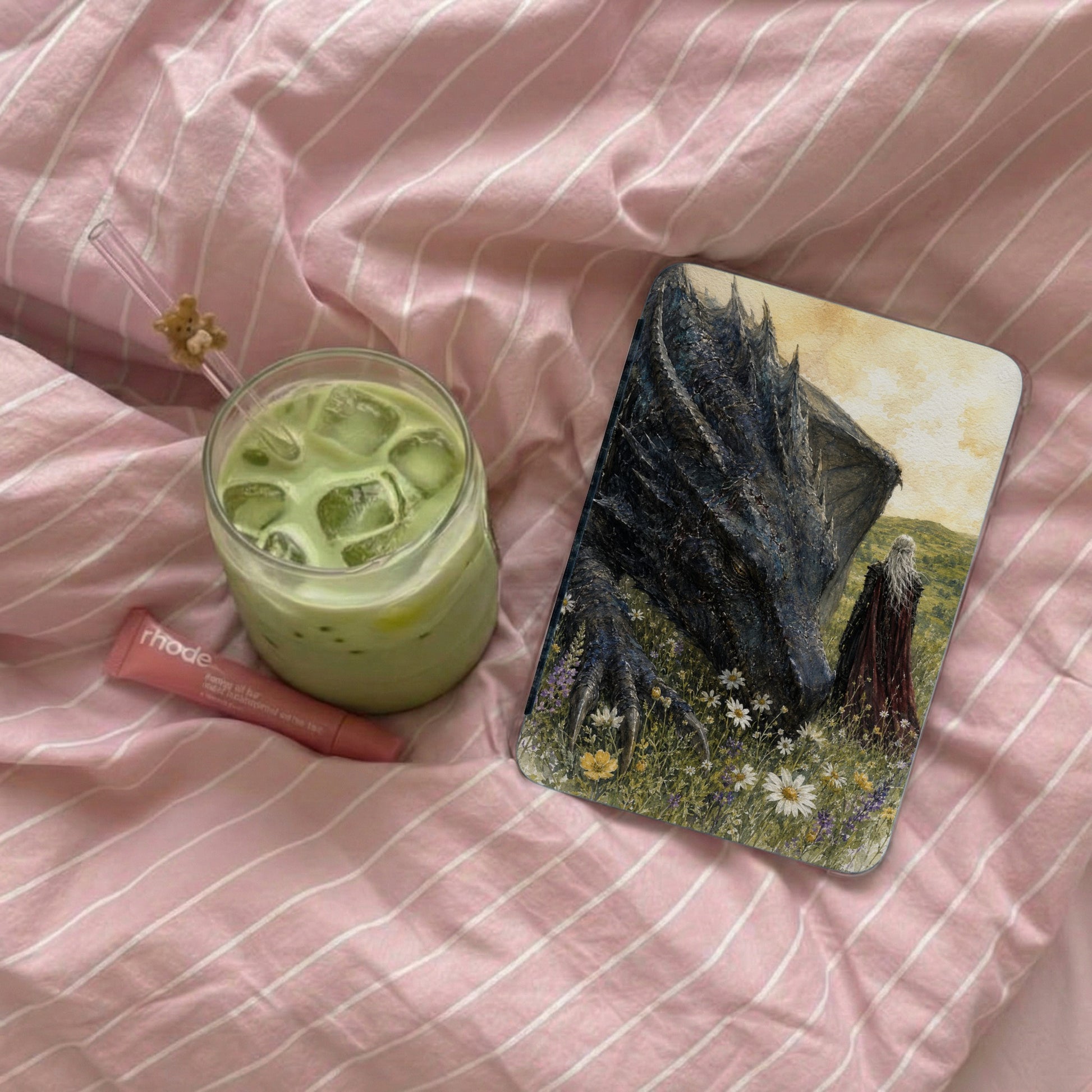 A glass of matcha, a lip balm, and a phone case with a dragon and figure.