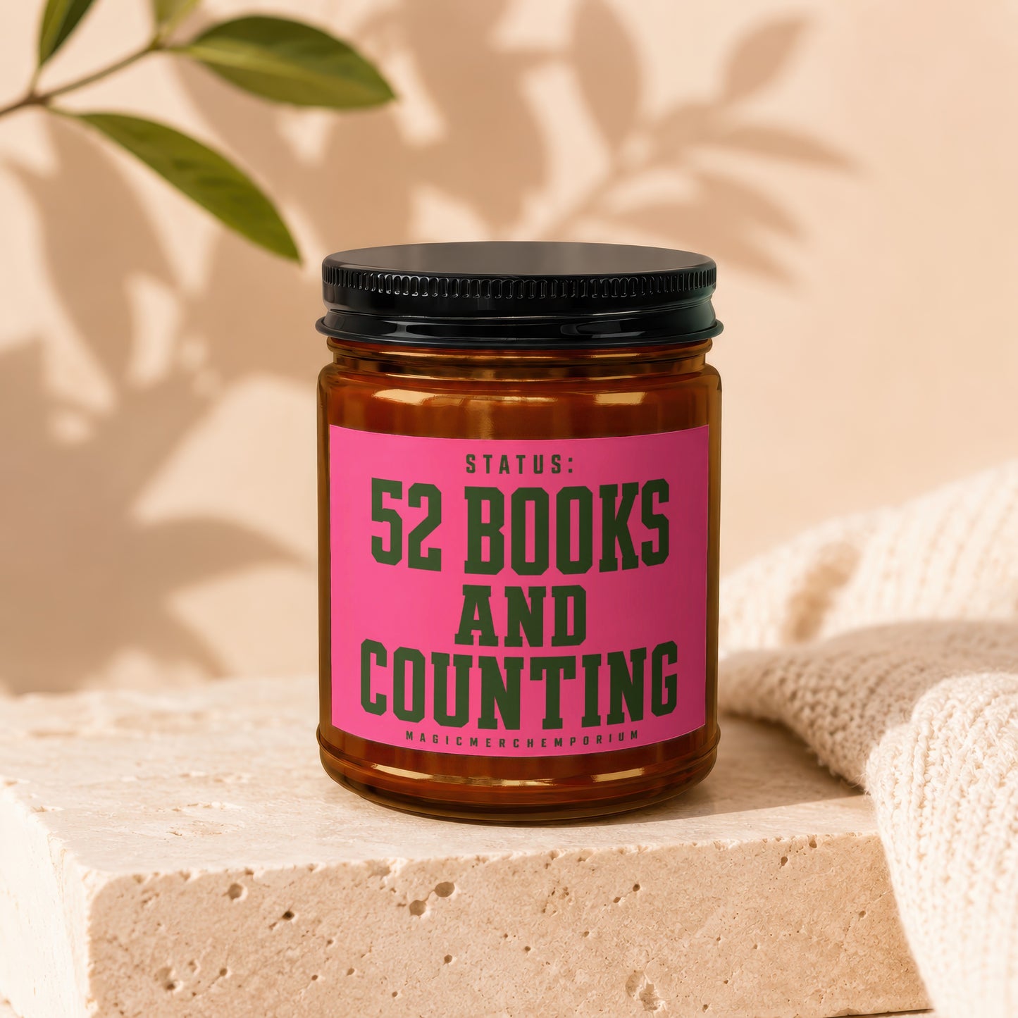 Amber jar candle with pink label reading "STATUS: 52 BOOKS AND COUNTING"