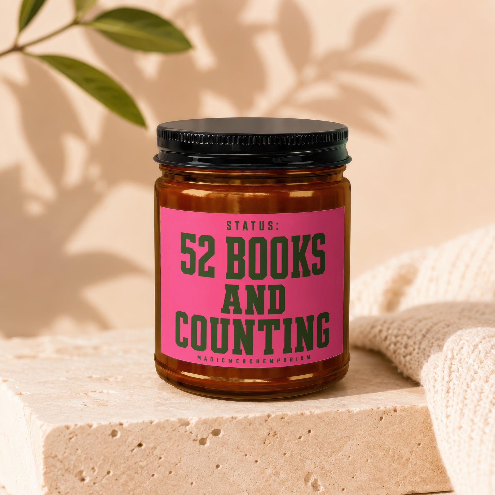 Amber jar candle with pink label reading "STATUS: 52 BOOKS AND COUNTING"