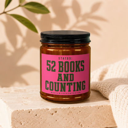 Amber jar candle with pink label reading "STATUS: 52 BOOKS AND COUNTING"