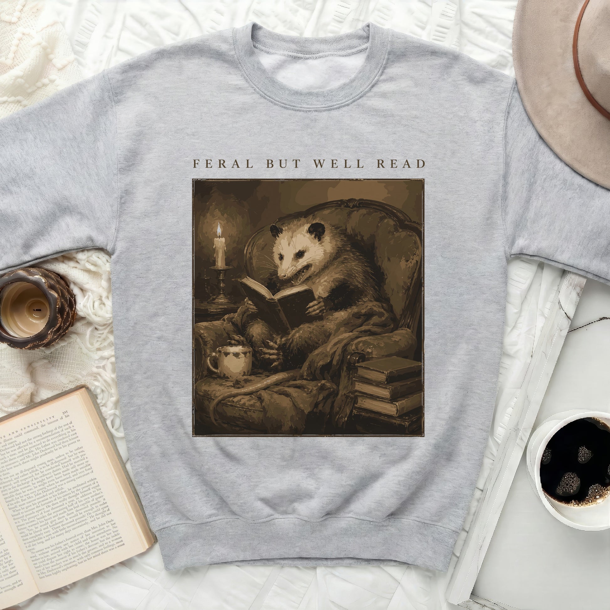 Gray sweatshirt with print of an opossum reading a book titled "Feral but Well Read".