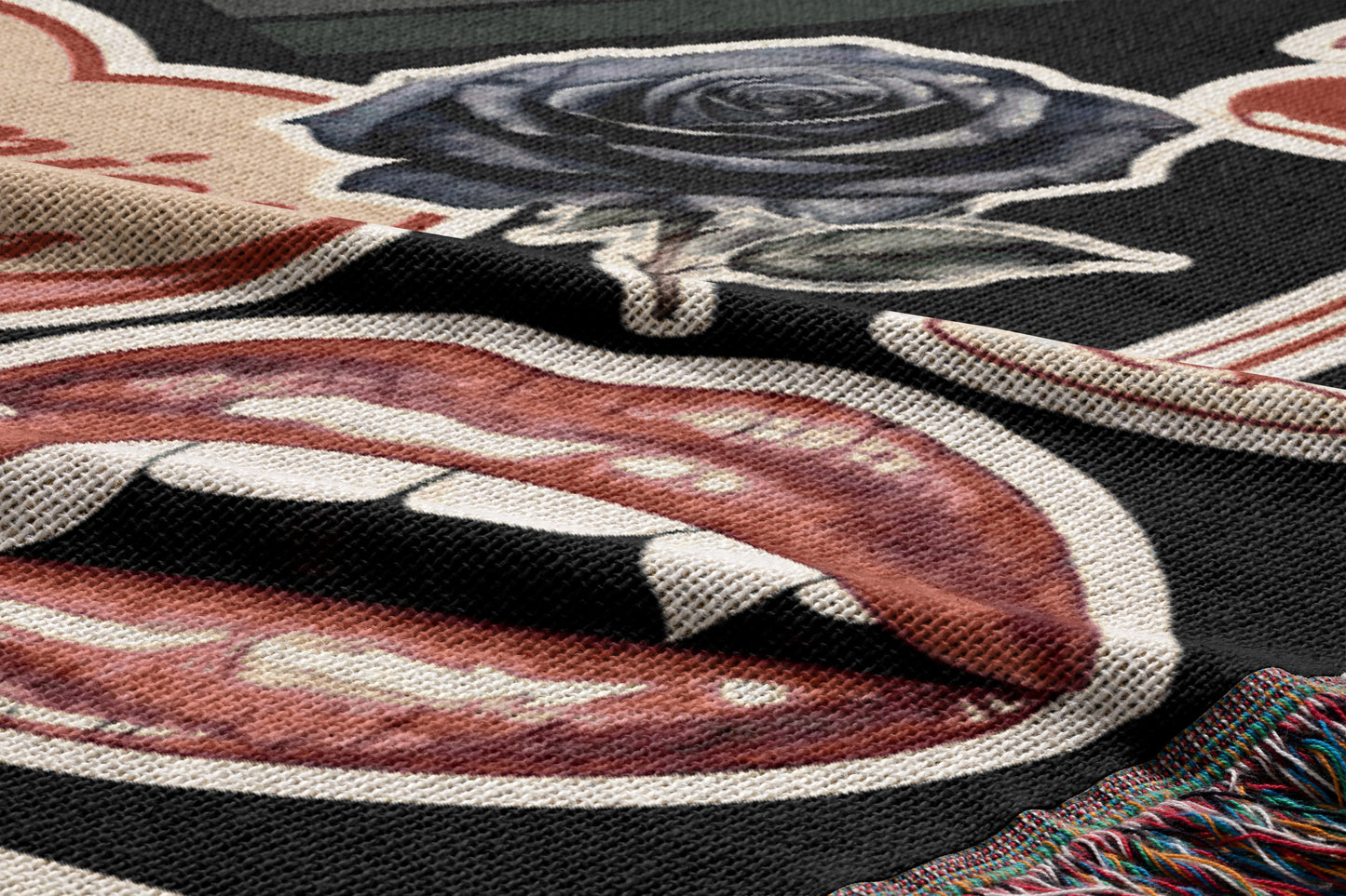 a close-up view of a textured fabric with a bold graphic design. The design includes a large, stylized depiction of a mouth with sharp teeth, a black rose, and a red tongue. The fabric appears to be a blanket or textile with a striking visual pattern.