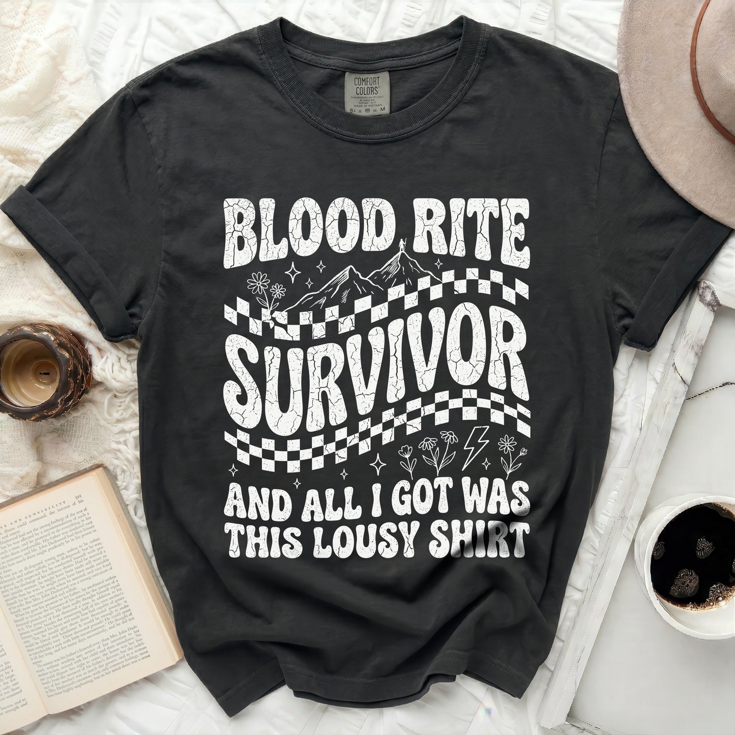 Black t-shirt with "Blood Rite Survivor" text, mountains, and checkered pattern.