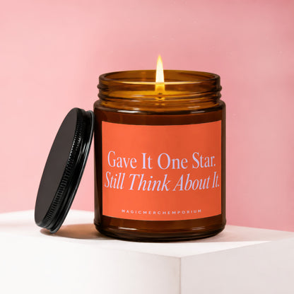 Amber glass candle with lit flame, black lid and orange label with text.