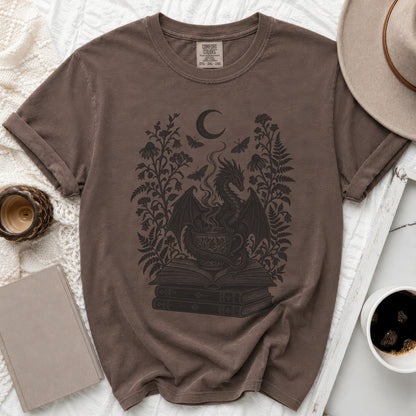 A brown crewneck t-shirt featuring a black line art graphic of a dragon, books, and flowers.