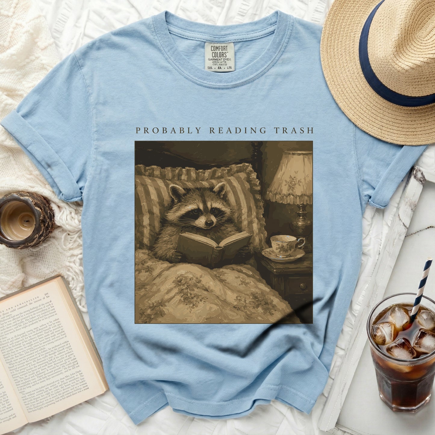 Light blue t-shirt with graphic of raccoon reading "PROBABLY READING TRASH".