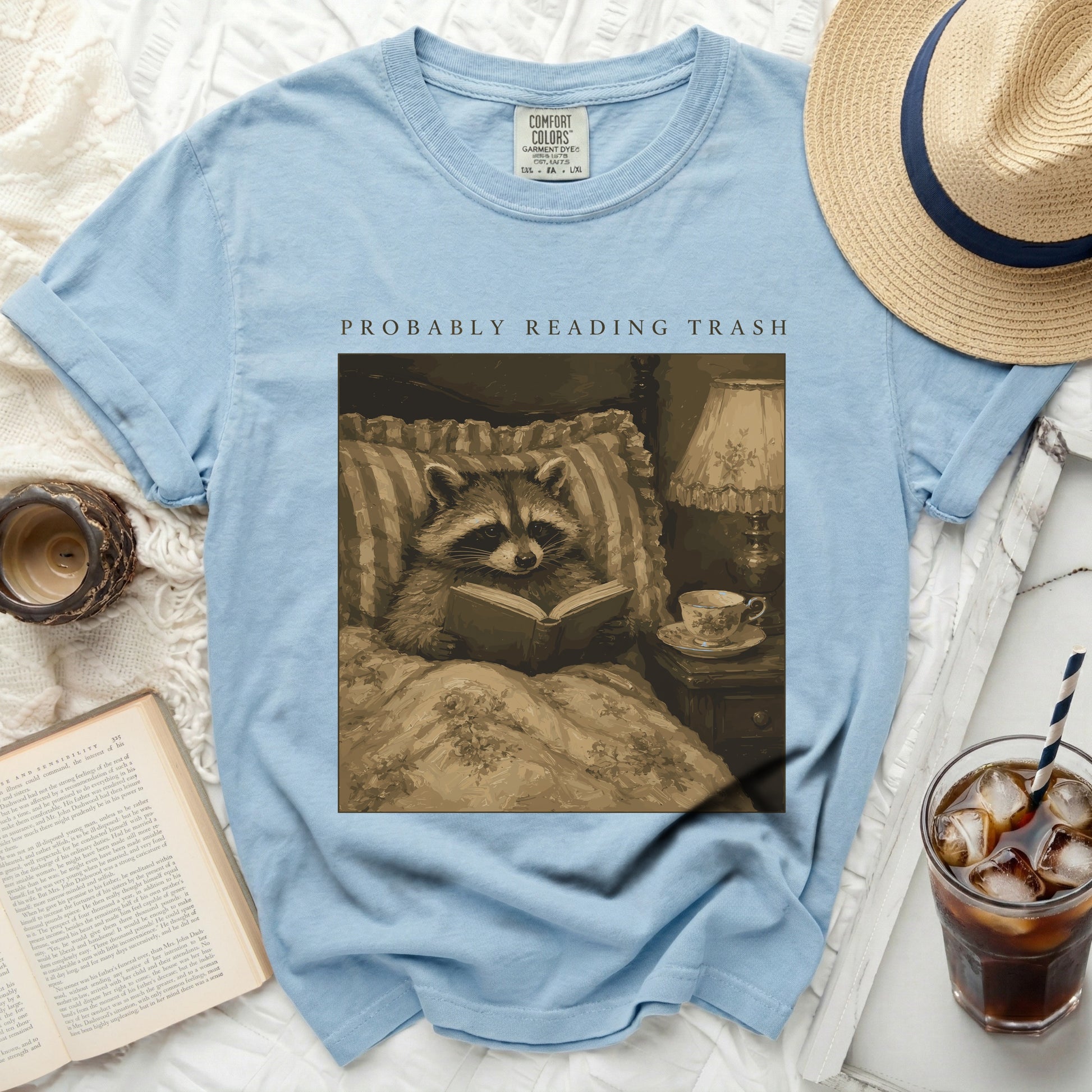 Light blue t-shirt with graphic of raccoon reading "PROBABLY READING TRASH".