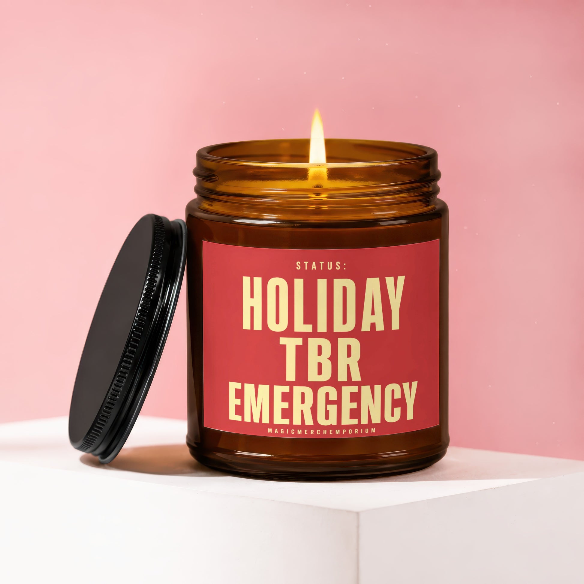 Amber glass candle burning with a red label saying "STATUS: HOLIDAY TBR EMERGENCY".