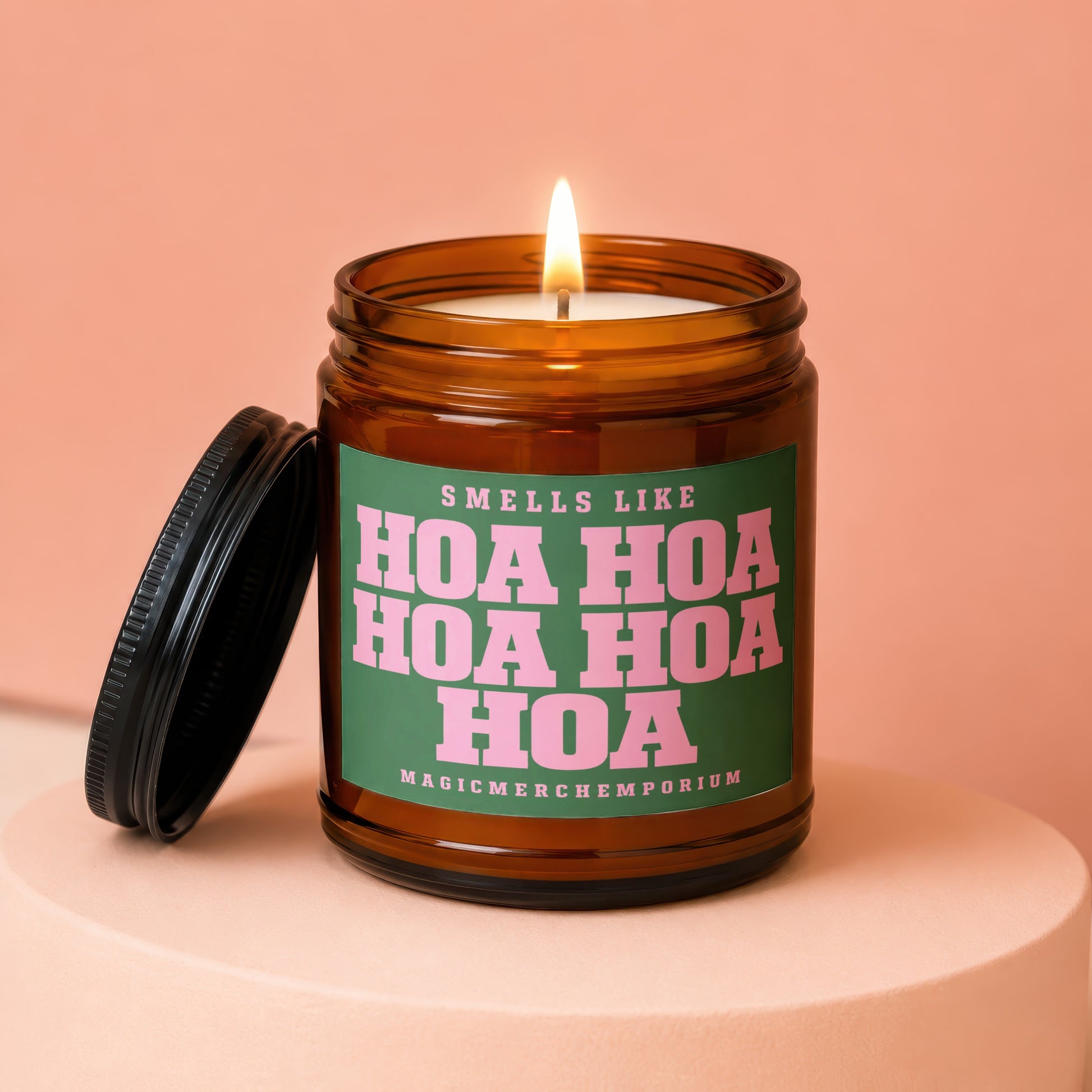 Amber jar candle with lit wick and black lid, label reads "Smells like Hoa Hoa Hoa".
