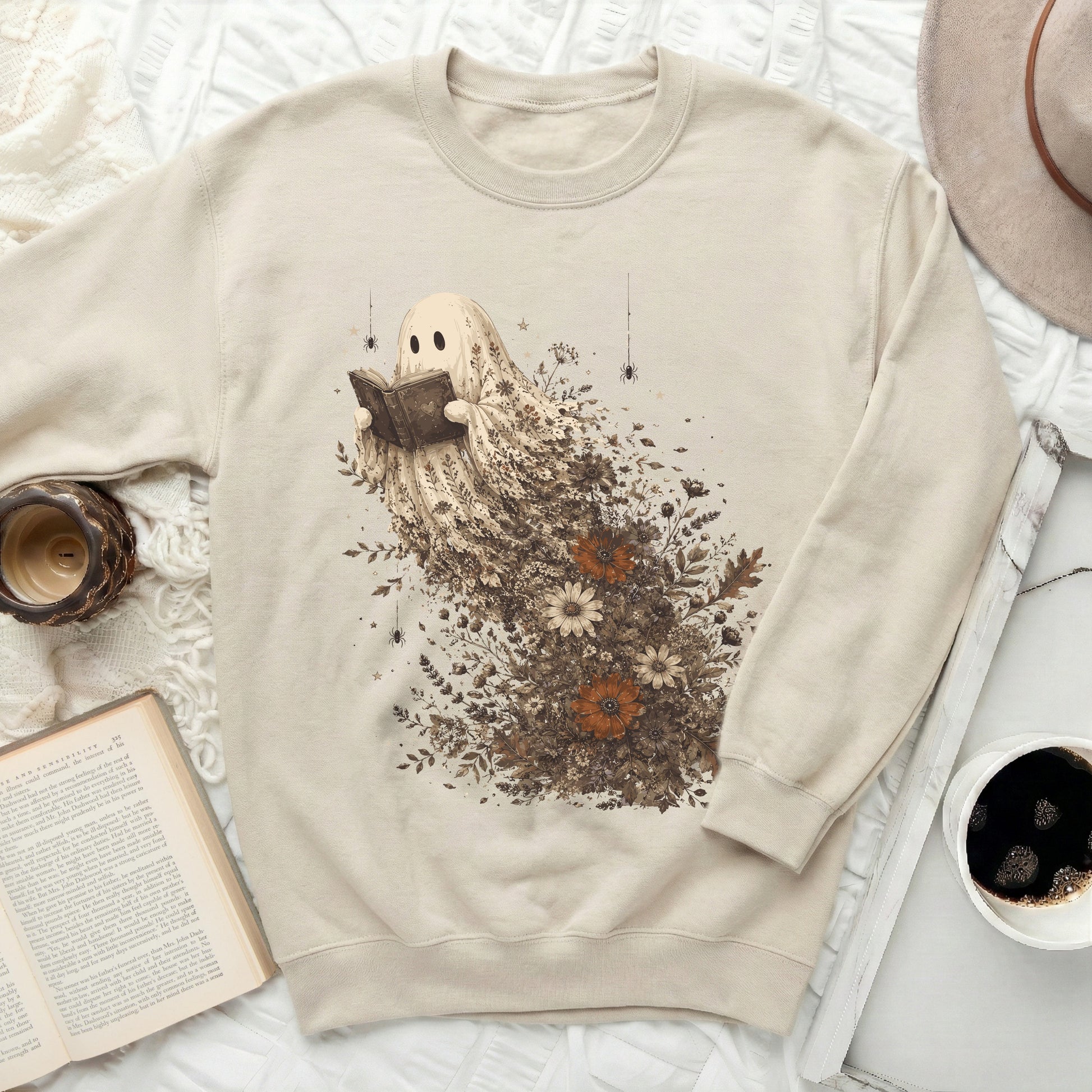 Cream sweatshirt with a graphic of a ghost reading a book, surrounded by flowers and leaves.