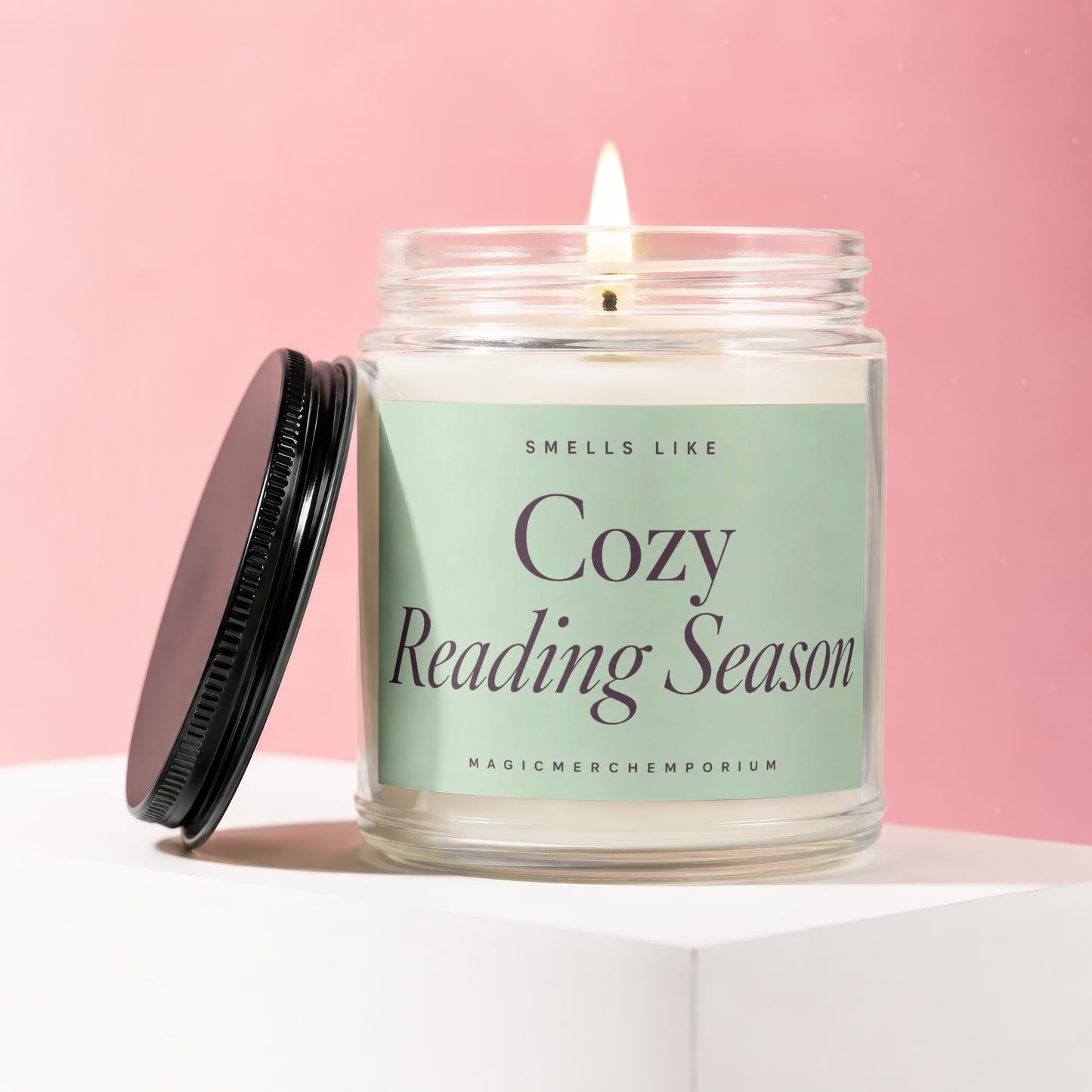 A lit candle in a glass jar with a black lid, labeled "Cozy Reading Season".