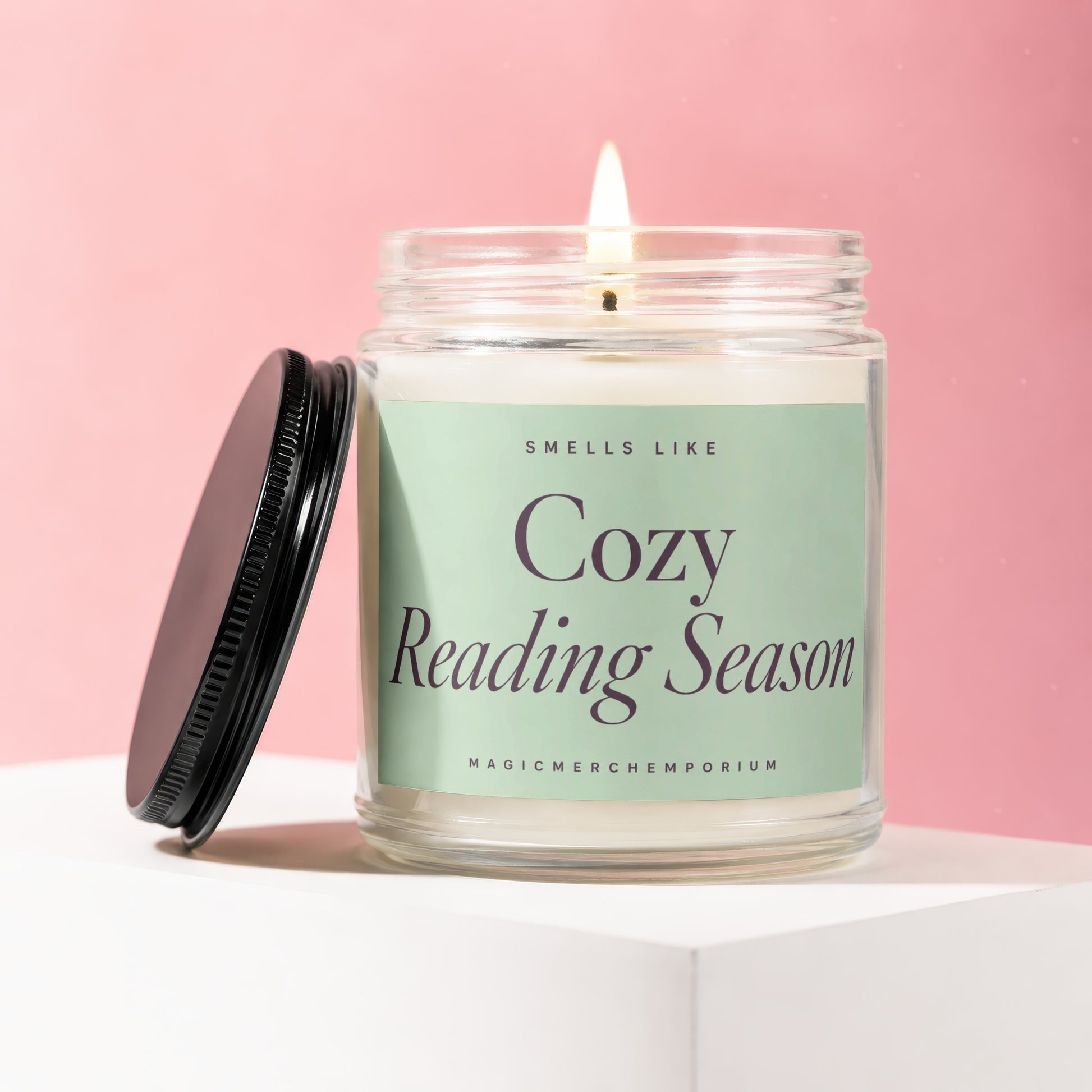 A lit candle in a glass jar with a black lid, labeled "Cozy Reading Season".