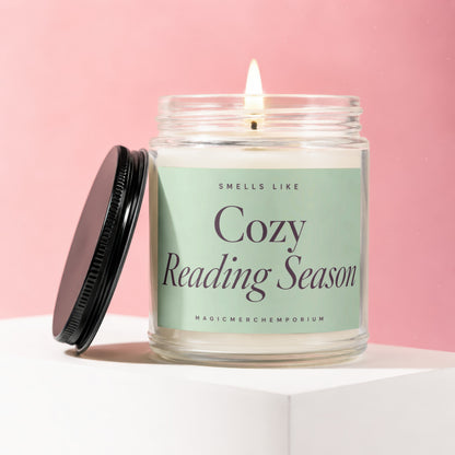 A lit candle in a glass jar with a black lid, labeled "Cozy Reading Season".